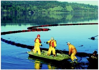 Workers clean up an oil refinery spill that polluted Anacortes Bay, Washington. The floating ring of absorbent pads trailing behind the boat is being used to contain some of the oil that has spilled.